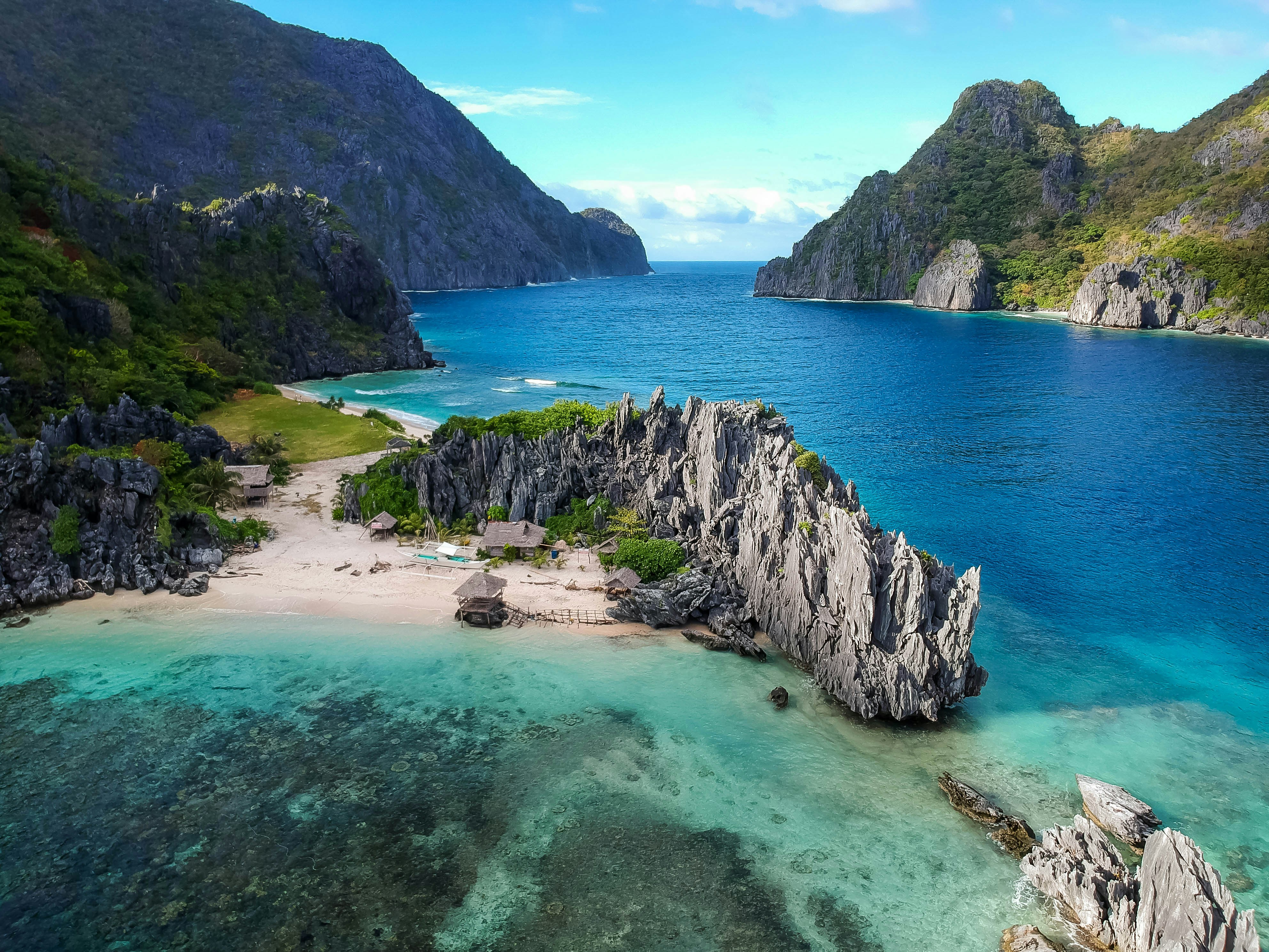 Aerial seascape of limestone karst cliffs, a white-sand cove, and turquoise water