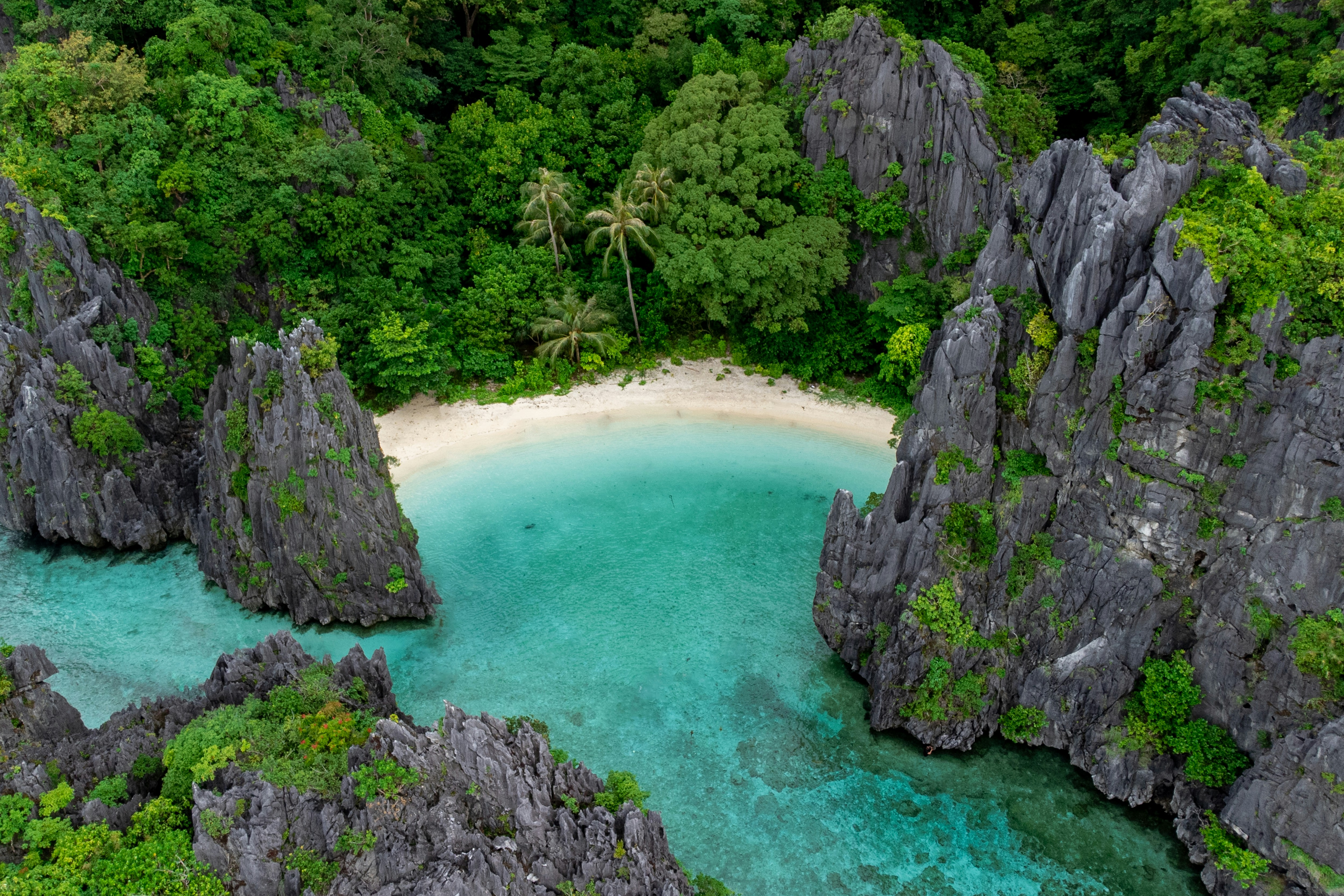 An aerial view of a hidden white-sand lagoon ringed by karst pinnacles and jungle