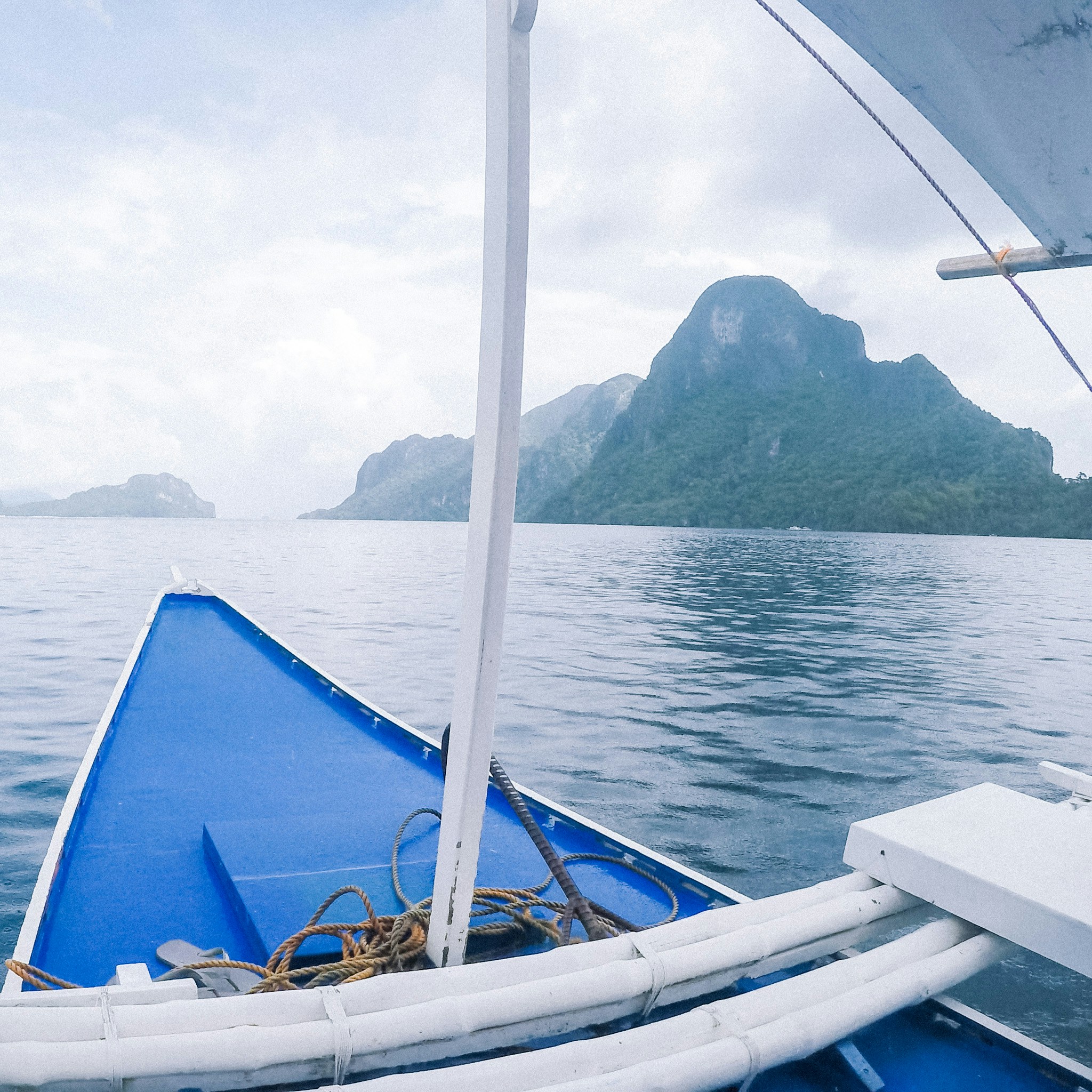 The bow of a traditional outrigger banca heading toward karst islands over turquoise water