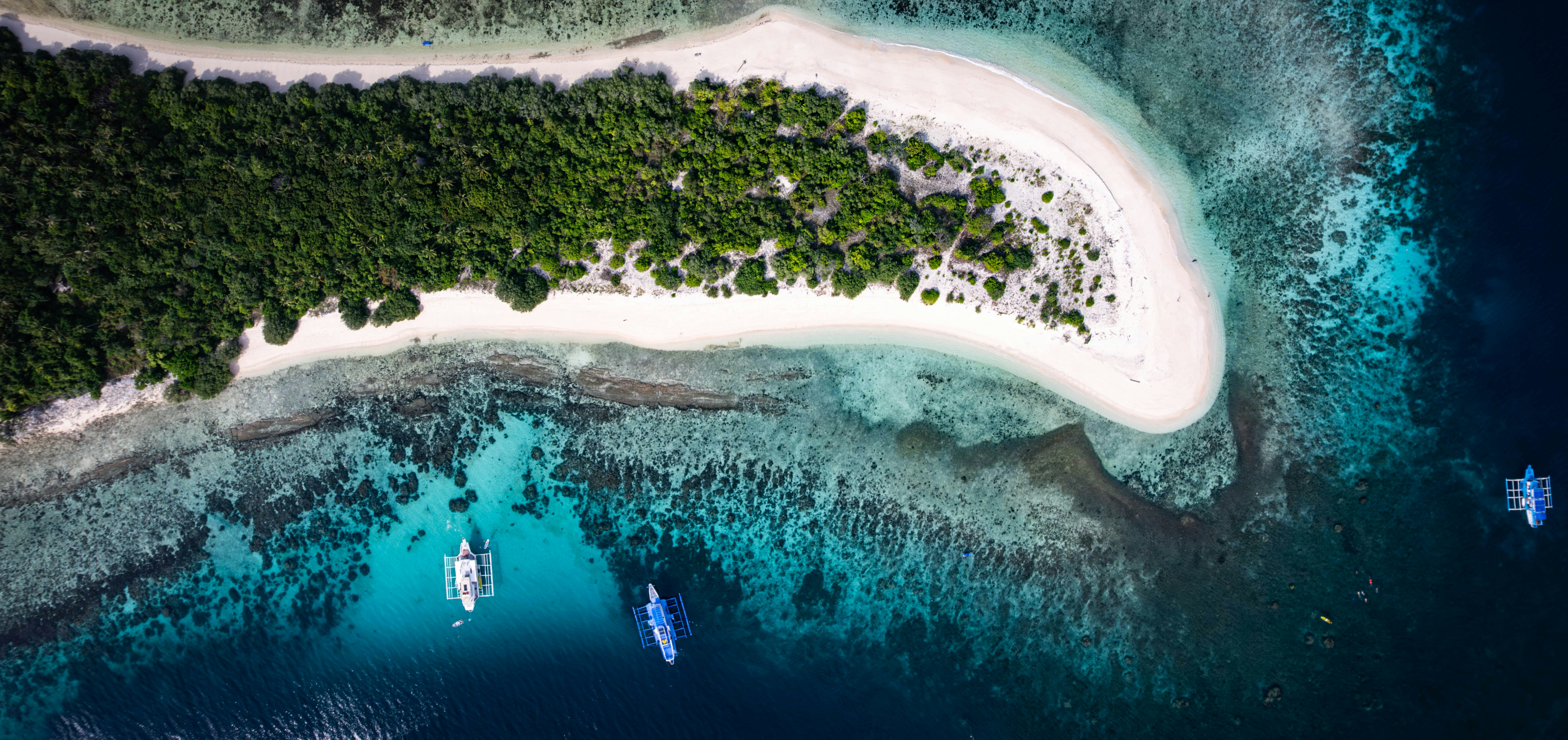 Top-down drone view of a tropical island coastline with reef and outrigger boats