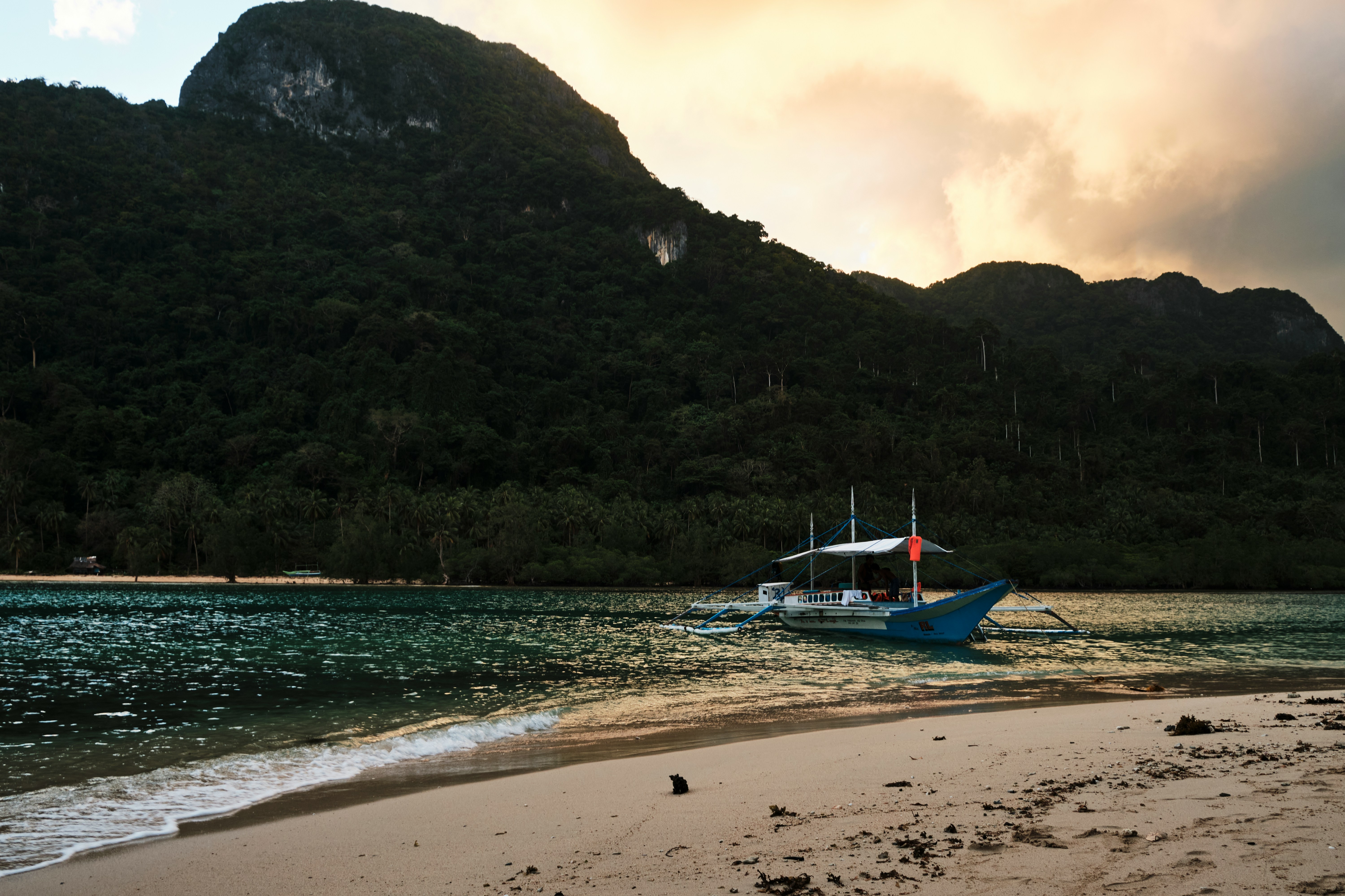 An outrigger boat beached at dusk under a warm sunset sky