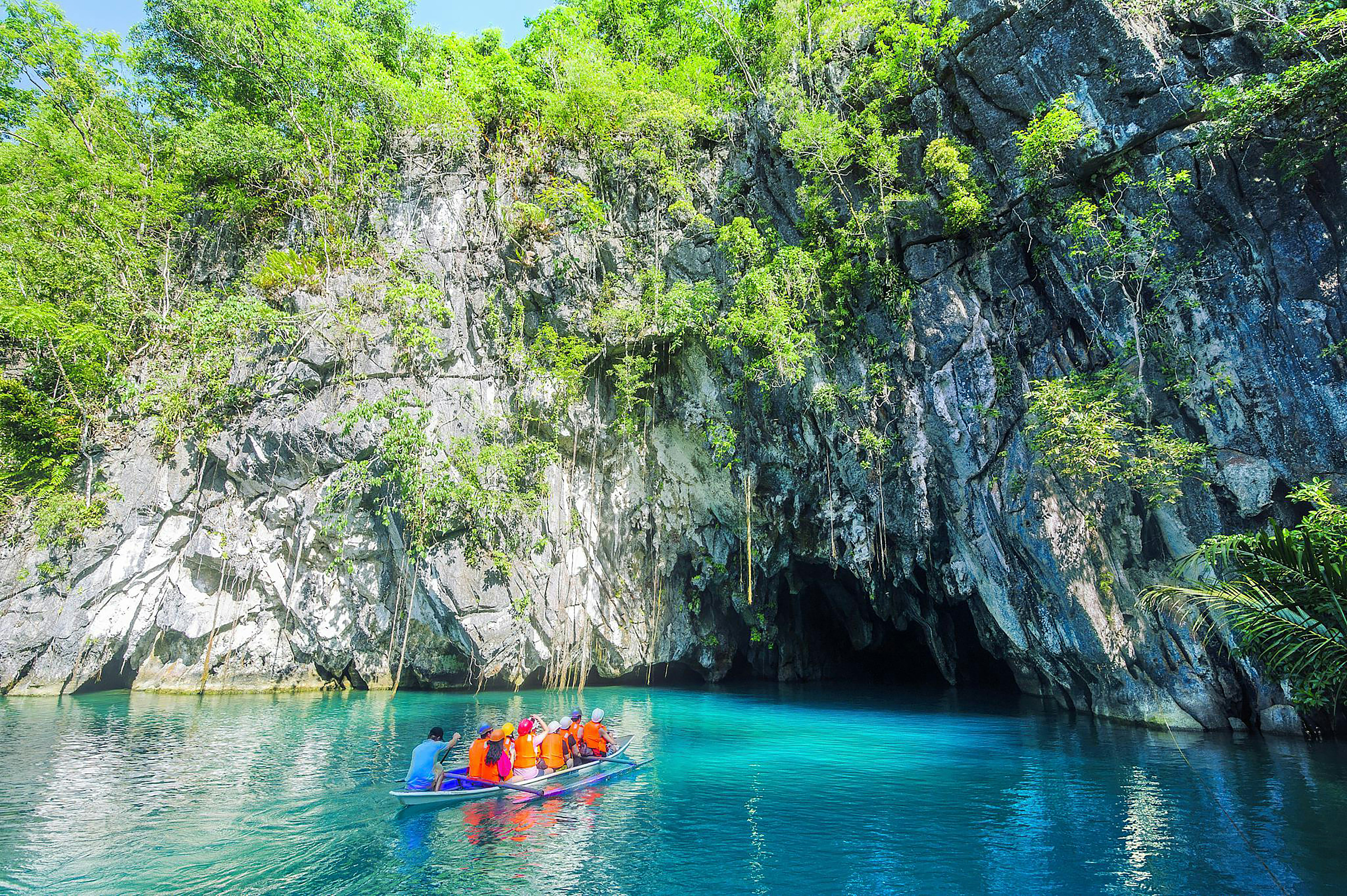 The cave-mouth lagoon entrance of a limestone karst river, a boat approaching in the distance